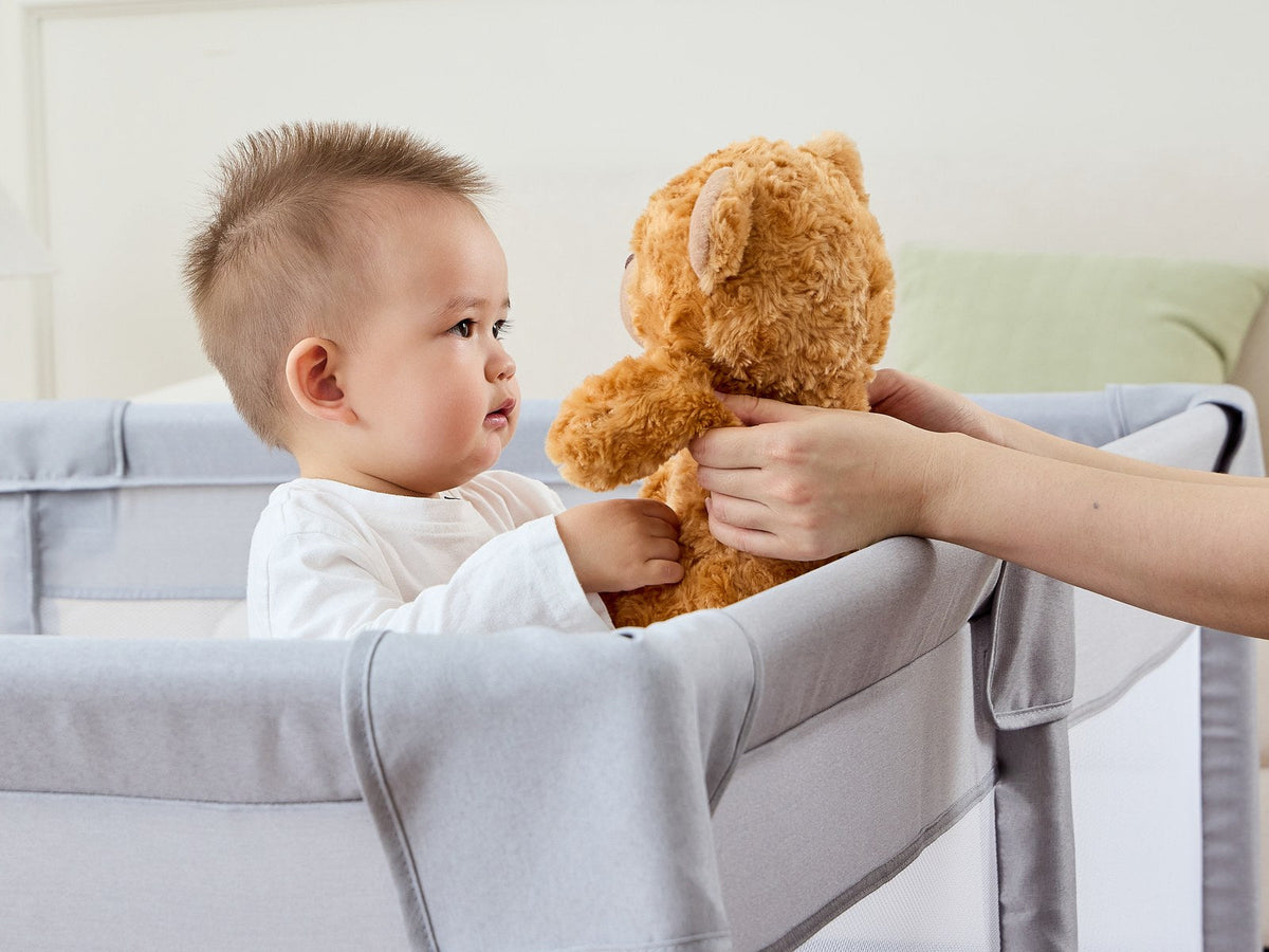 ベビーサークルの中で家族からぬいぐるみを受け取る赤ちゃん